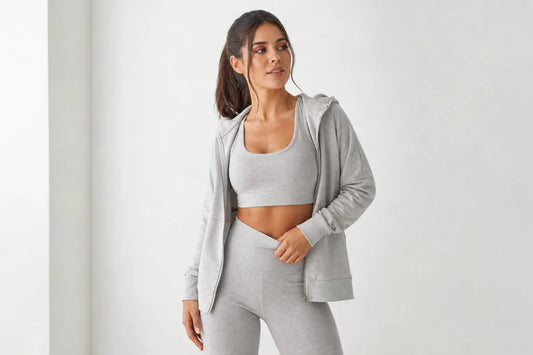 Mulher sorrindo em um conjunto de moletom cinza claro, em um estúdio com fundo branco.